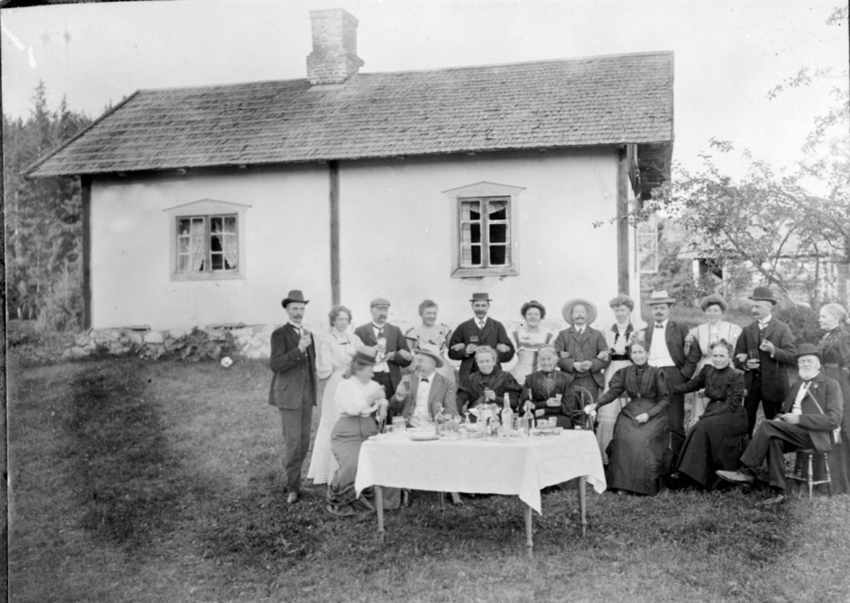 Anno Domkirkeodden, Festlig lag med mye folk utendørs, bord med flasker og glass. Rappet tømmerbygning.