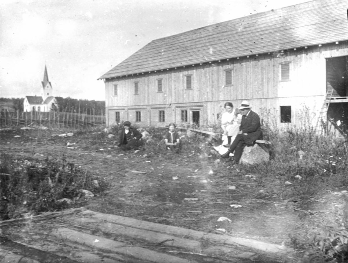 Anno Domkirkeodden, Gruppe personer foran ny låvebygning på Flisaker gård, Veldre, Ringsaker. Veldre kirke i bkagrunnen.