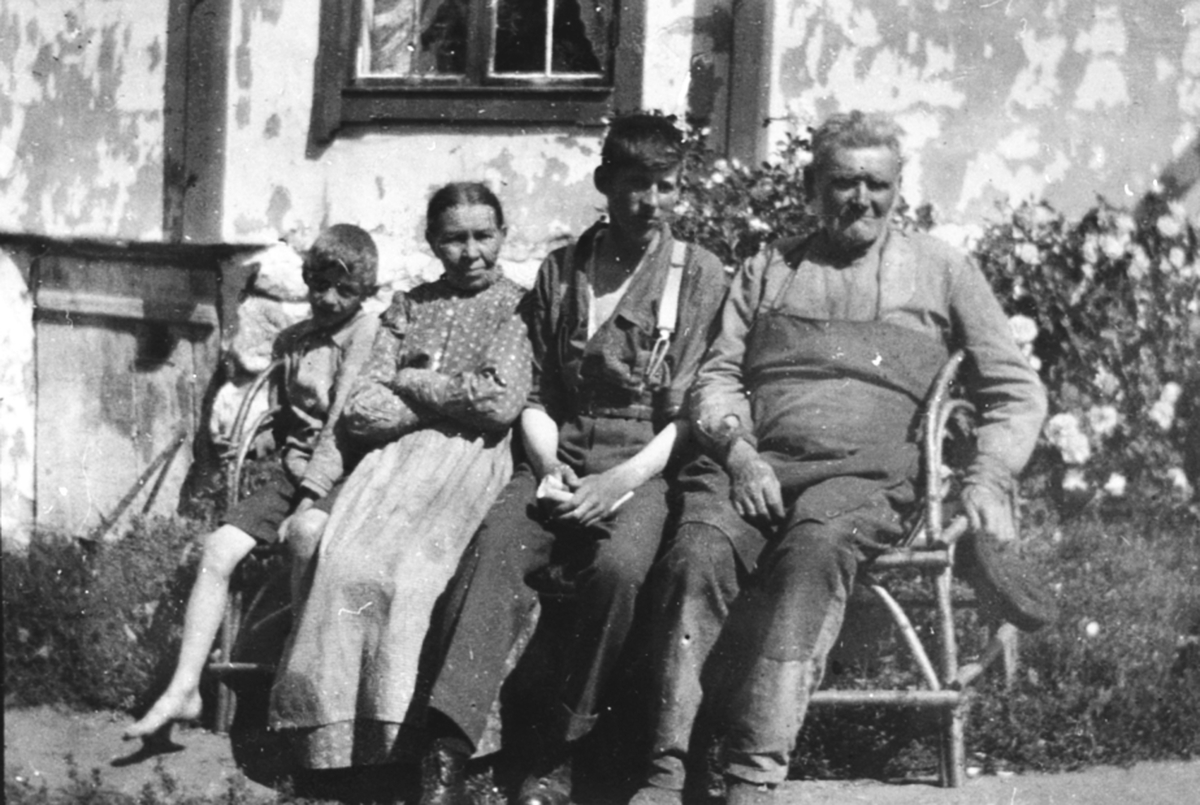 Anno Domkirkeodden, 4 personer sitter utenfor huset i Sundby lille, Skredderbakken, Helgøya. Fra venstre Asbjørn Solmund Aas f. 1912, Marit Jensdatter (1855-1939), Leif Sæhlie, Johannes Akselsen (1844-1926).