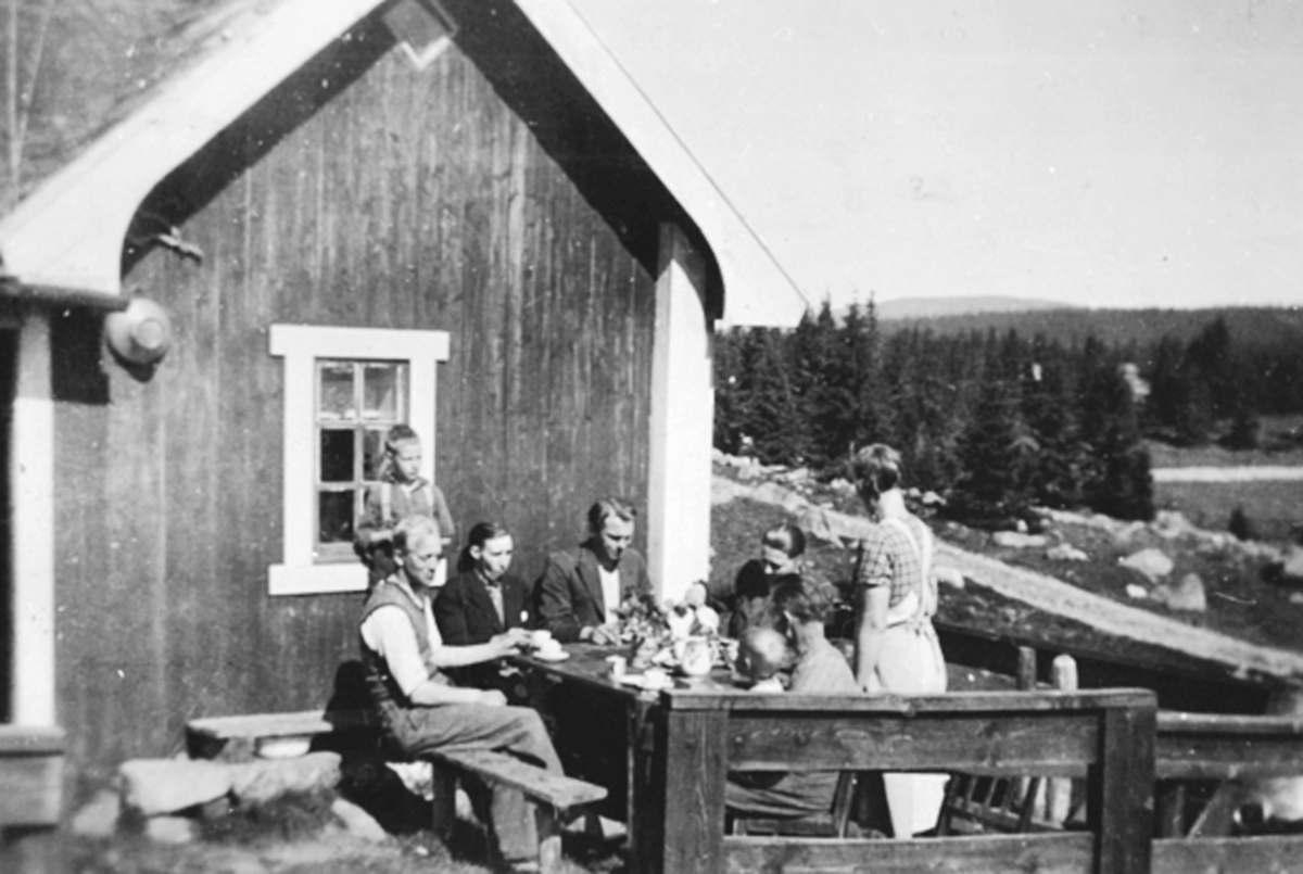 Anno Domkirkeodden, 8 voksne og barn rundt kaffebordet utendørs på Olshølen seter Brattberg. Sverre Hovland, Nils Hovland, Hans Haugen, Anne Dortea Haugen, Gudrun Hovland, Sigurd Hovland med Gunnar på fanget, Ringsakerfjellet.