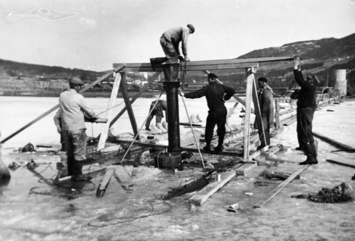 Anno Domkirkeodden, Bygging av vanninntak, pumpestasjon, inntaksil settes på plass, Hedmark Tørrmelk, Tine, Brumunddal. 8 menn arbeider.