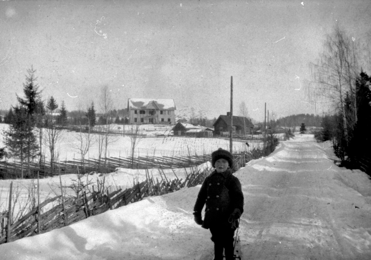 Anno Domkirkeodden, Den gamle Dæhli skole, Nes, Hedmark. Ny skole ble bygget i 1917. Husa i forkant av skolen er vel husmannsplassen Korslund, som ble revet i 1915-16. Ukjent gutt med kjelke i forgrunnen.