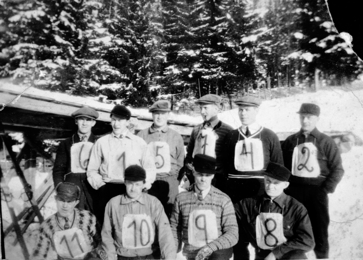 Anno Domkirkeodden, Gruppe skihoppere med startnummer. Veldre gubbelag, Dalhusbakken, Veldre. Foran fra venstre er Martin Larsen, Nils Bjørksveen, Gudbrand Frydenlund, Olaf Høgsveen. Bak er Mæhlum, Ottar Lunde, Jørgen Opsahl, Eivind Glestad, Aksel Johansen, Johs Finstad.