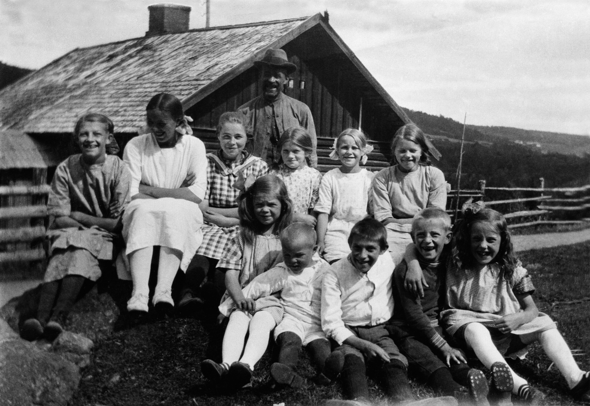 Anno Domkirkeodden, Alf Prøysens søskenbarn fra Oslo og nabounger foran Prøysenstua i Præstvægen. Alf's far Olaf Andreassen bak. Foran fra venstre er Olaug Strandli, Harald Larsen, Olaf Evensen, Alf Olafsen, Elinor Strandli. Andre rekke er Margit Olafsen gift Tverråen, Hanna Stensåsen gift Langård, Olga Sletten, Thora…