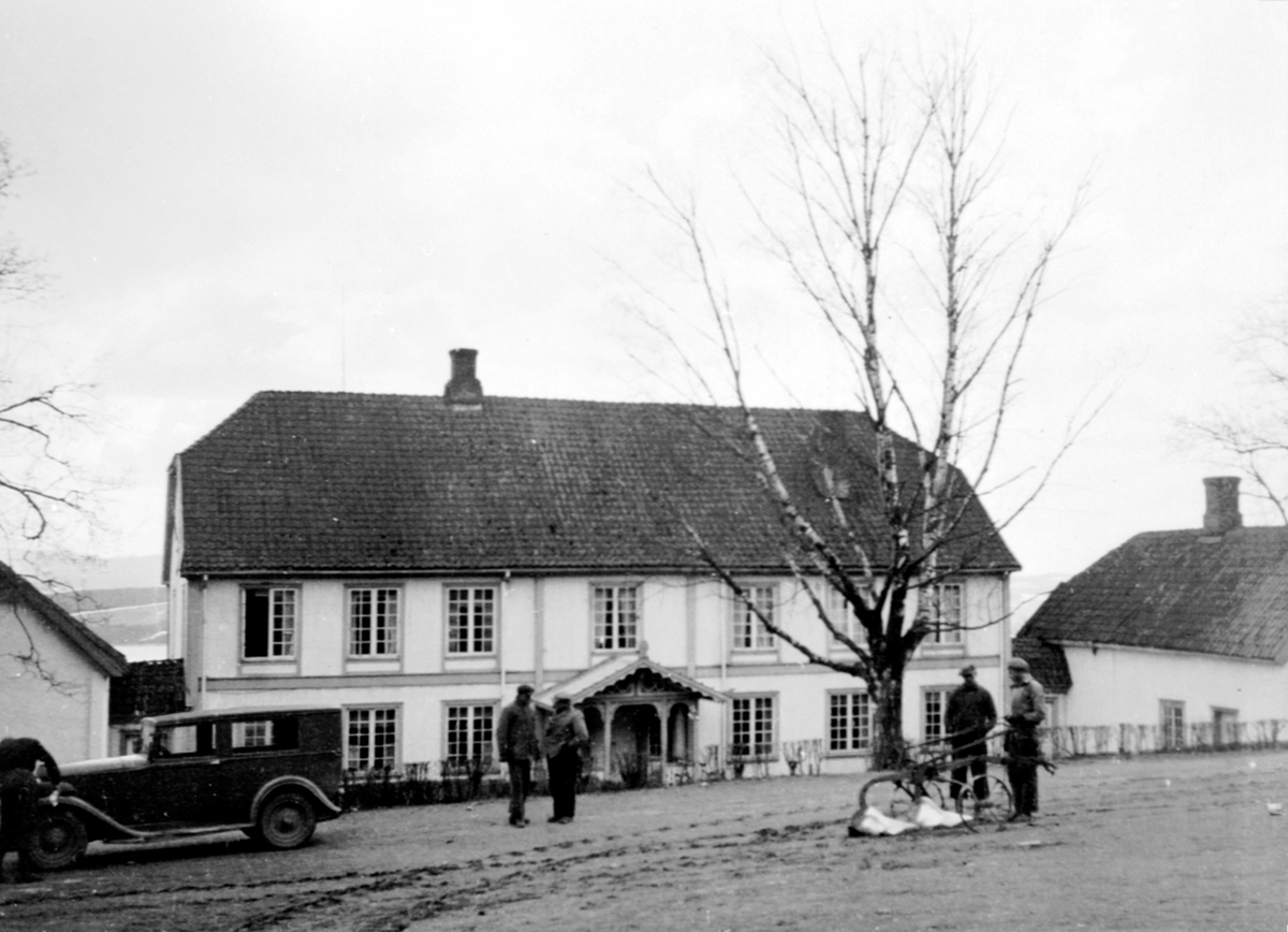 Anno Domkirkeodden, Hovedbygningen på Hovelsrud, Helgøya sett fra vegen. Bil og 5 karer i forgrunnen. Plog.