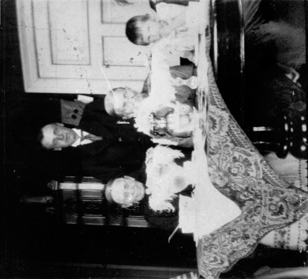 Anno Domkirkeodden, Interiør fra stue på Fossum, Nes, Hedmark. Bord med duker. Ved bordet er Oline Fossum, Marie Fossum, Finn Fossum. Den siste er ukjent.