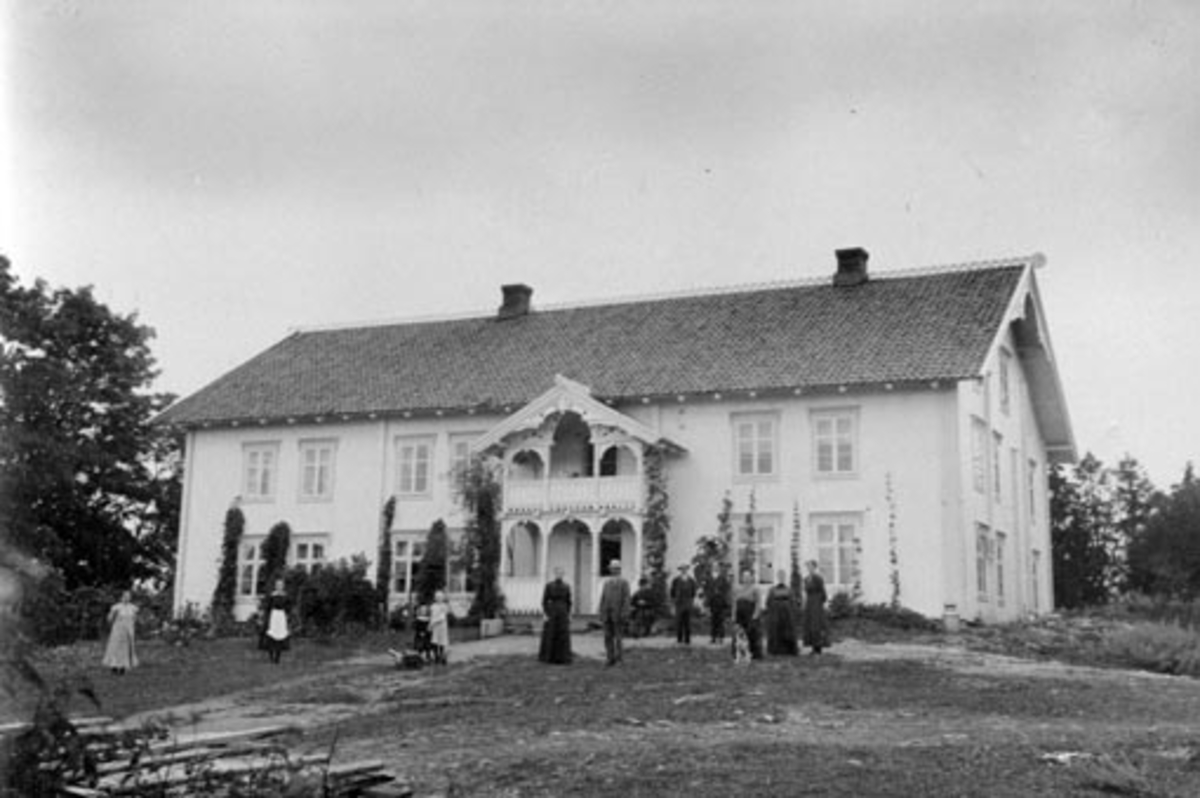 Anno Domkirkeodden, Eksteriør gardsbruk, Hulleberg nedre, Nes, Hedmark. Gruppe mennesker foran huset. Blant andre Martinius Hilstad (1834-1929) på trappa, Martha (1864-1944) , Andreas (1858-1933), Ole (1901-1968), Nils (1904-1926) og Aslaug Malmfrid Børke f.1911.