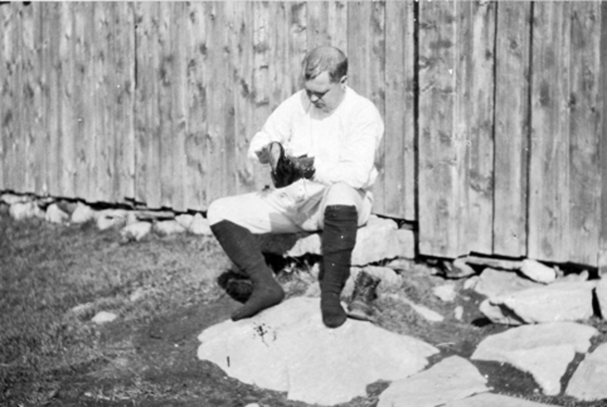 Anno Domkirkeodden, Portrett, Jørgen Larsen pusser sko i bare undertøyet. Foran Grythesetra i Furnesåsen. Skopuss.