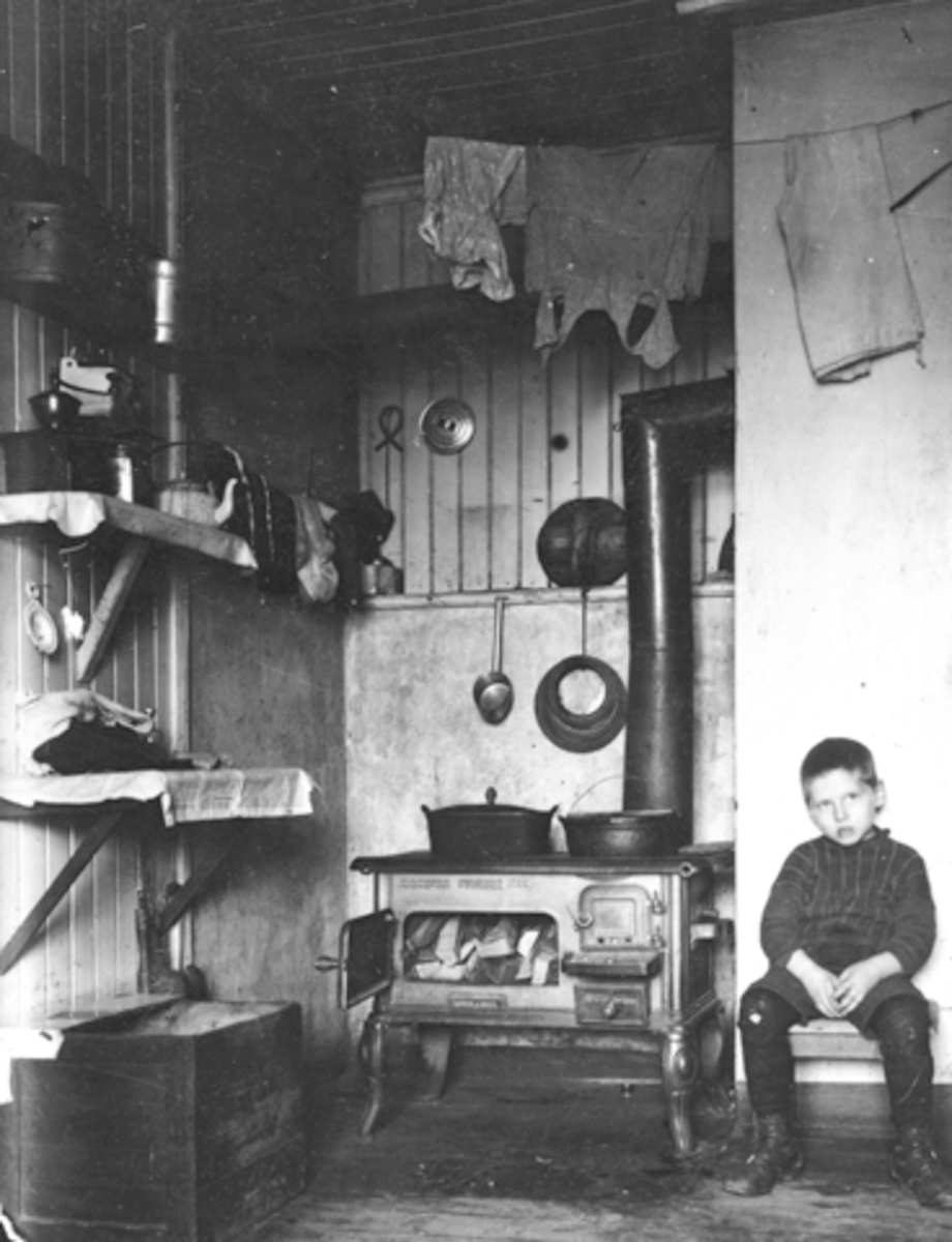 Anno Domkirkeodden, Interiør, kjøkken, liten gutt på krakk ved komfyr fra Moelven støberi NO 22, ca. 1900-05.