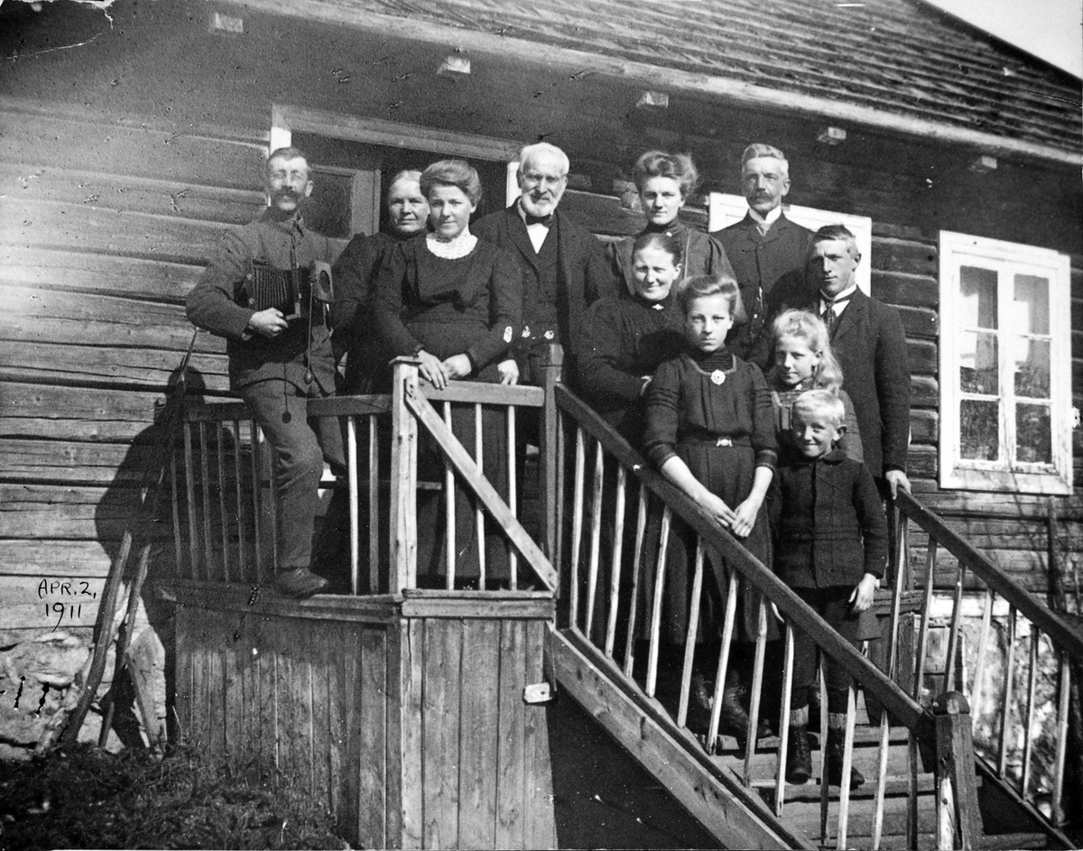 Anno Domkirkeodden, 2. april 1911 ble Øvern, Stavsjø, Hedmark fraflyttet. Familien på trappa. Foran foreldrene står Gunnar, Martha, Petra og Gudbrand. De voksne jentene er trolig to av de tre eldste døtrene. Det eldre paret bak er ukjent. Fotograf med kasse til venstre.