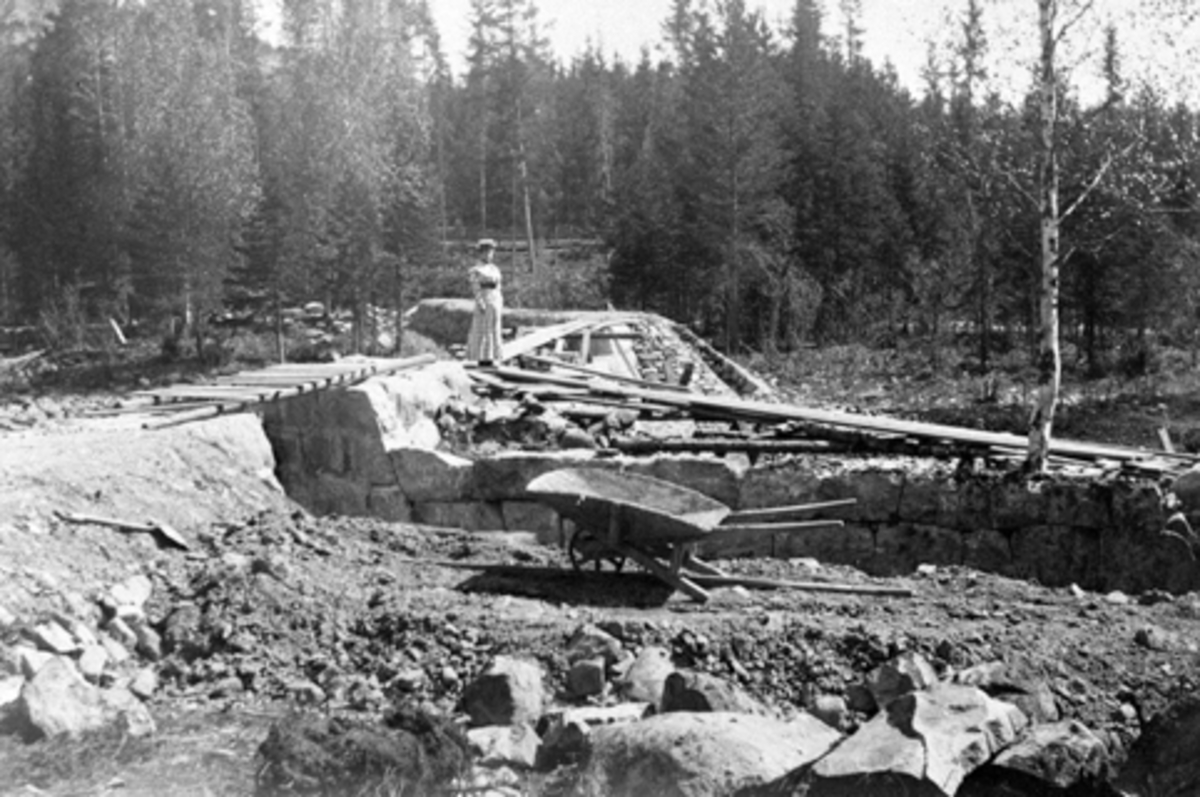 Anno Domkirkeodden, Utgraving av tilførselkanal til Moelv kraftstasjon, ble bygget for Moelv Cellulosefabrikk ca. 1907-1909. Kanalen var 1600 meter lang og kraftverket produserte ca. 800kw. Steinsatt del av kanal, bru, ukjent kvinne.