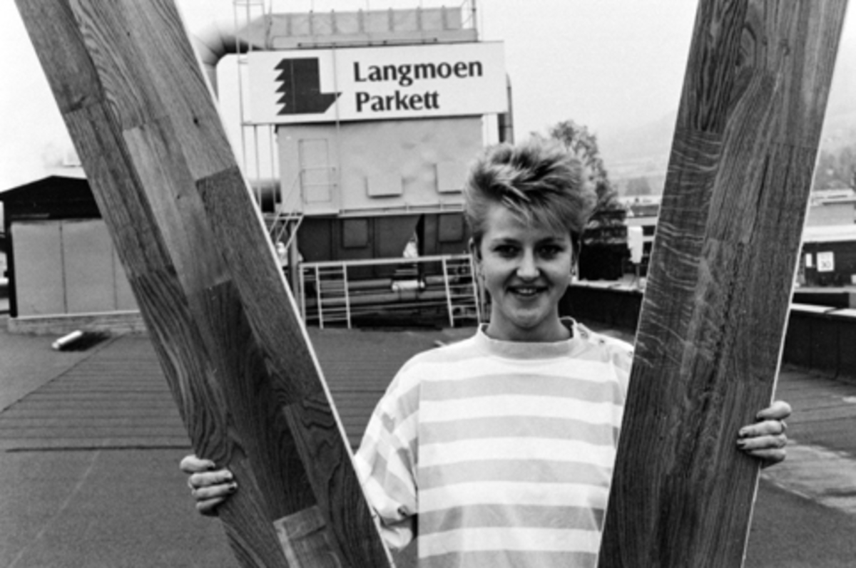 Anno Domkirkeodden, Berger Langmoen A/S, Norske Skog, Brumunddal. Interiør, parkettfabrikken. Produksjon av parkett, Elin Lunde med ferdig produkt på fabrikkens tak, logo på vegg bak.