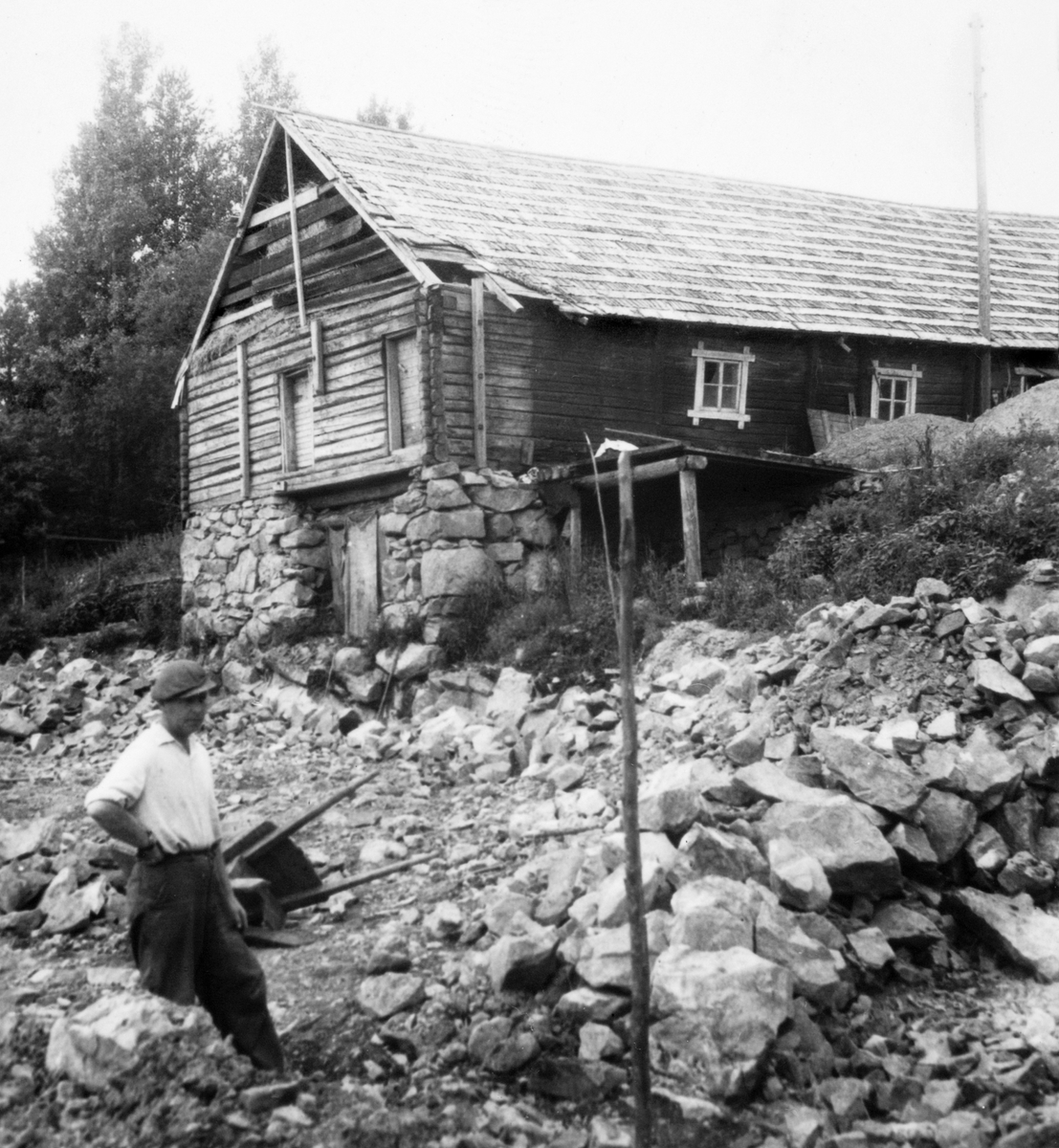 Anno Domkirkeodden, Gardbruker Hans H. Medlien med spett og trillebår i steinura der gamlelåven på Medlien gård, Ringsaker stod. Grunnlaget for nyfjøset er i gang. 1960.