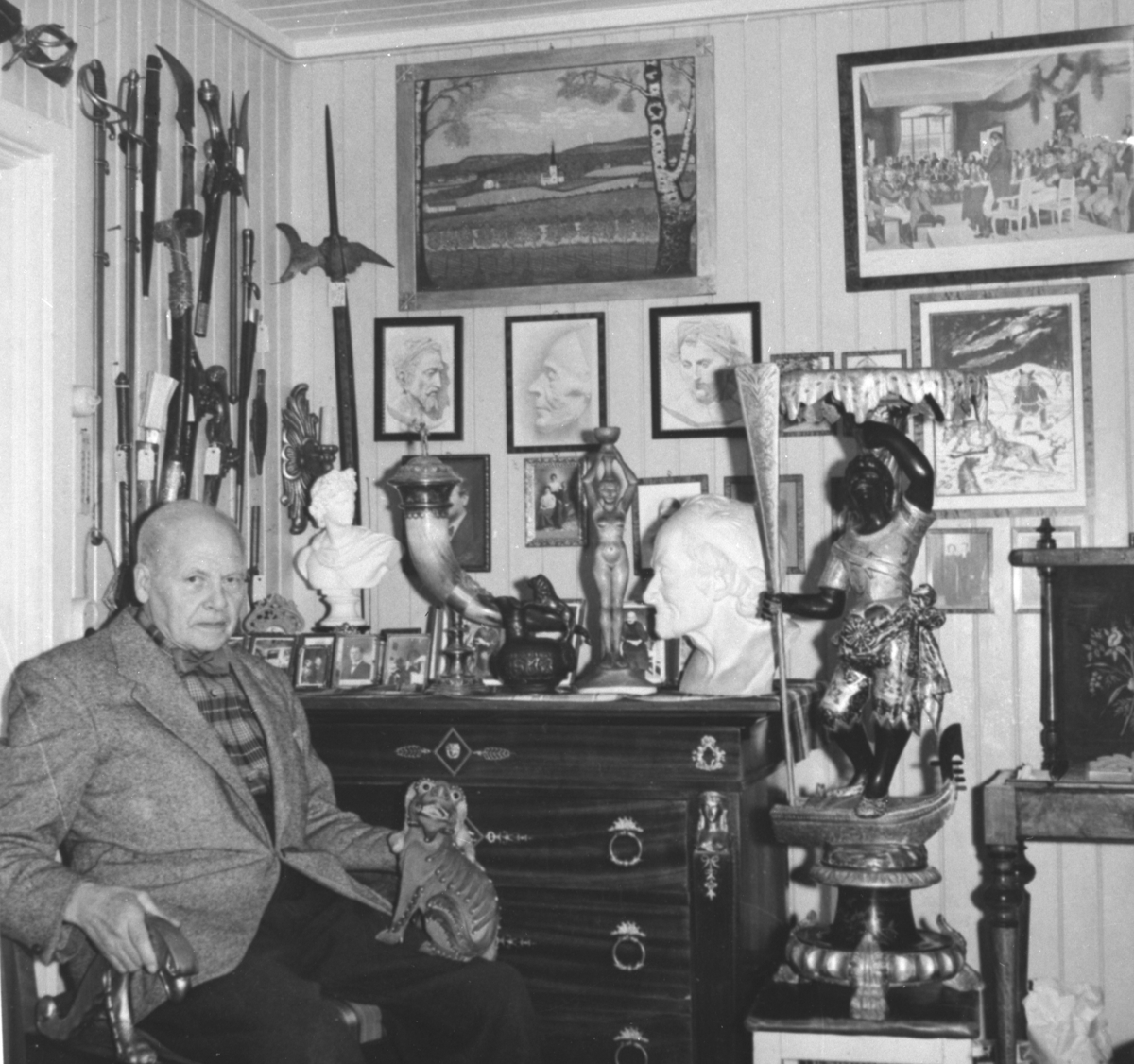 Ukjent, Ukjent eldre mann, fotografert foran større samling av antikvariske våpen og andre samleobjekter.