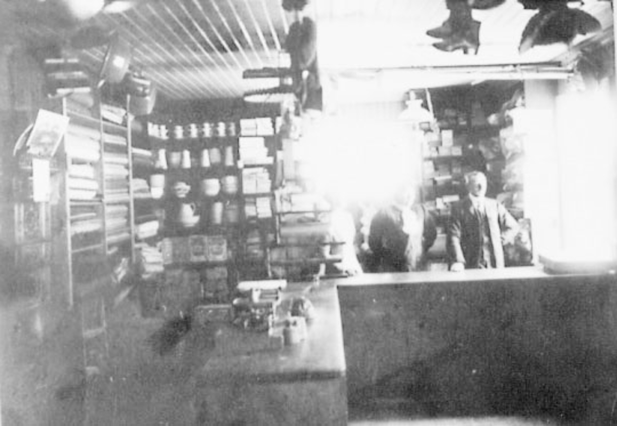 Normann Helger, INTERIØR: FORRETNING, BUTIKK, SKO, TEKSTILER, VEKT M. M. , GRUPPE: 3 BAK DISKEN, KAREN HESTNES, FRU SIGNE LUND, INNEHAVER: KRISTIAN HESTNES. Arnesveen landhandel på 1930-tallet. Flere opplysninger se boka "Handelssteder i Stange" skrevet av Jan Arne Berg, utgitt av Stange Historielag 2012