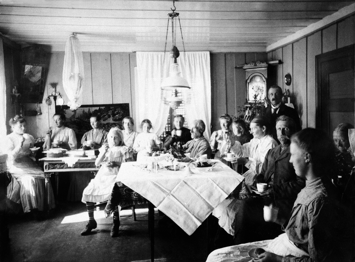 Normann Helger, INTERIØR: STUE, GRUPPE: 15 RUNDT BORDET, HAUKAASEN NORDRE, . FRA VENSTRE: MARIE HESTNES, KAREN HESTNES, ELLEN HESTNES, VED BORDET FORAN: SERINE HAUKAASEN, GUNDA GUTHUS, GUDRUN GUTHUS, FRU SKREPPERUD, ANDERS A. HAUGAASEN, OLGA HESTNES, MARGIT HAUKAASEN, MARGTRTHE HAUKAASEN, ANDERS HAUKAASEN, ANNE MA…