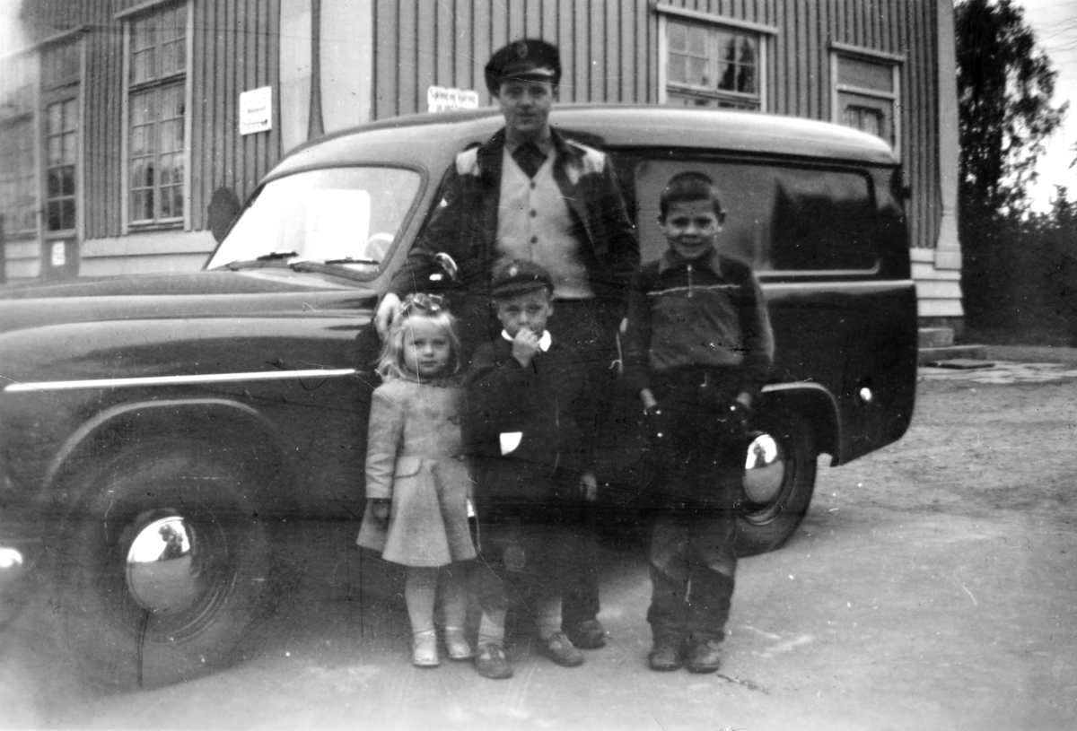 Ukjent, Drosjesjåfør Arne Gustavsen foran drosjen sammen med Liv Gustavsen, Lars Ingel, Per Arne Gustavsen. Tatt på Tangen stasjon ca. 1955. En lukket varebil, trolig Commer.
