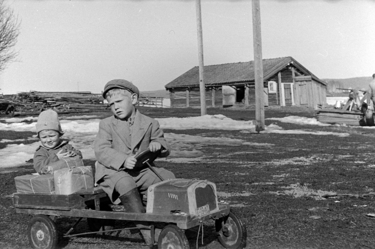 Adolf Skjegstad, ODD KJELL SKJEGSTAD, 6 ÅR ER SJÅFØR PÅ LEKEBILEN, OG ANNAR SJEGSTAD SITTER PÅ LASTEPLANET. LEKEBIL, TRÅKKEBIL, BARNELEKE, UTHUS GARD, STANGE, OKTOBER 1941. FAREN A, SKJEGSTAD HADDE BILDET OVER SENGA SI DA HAN SATT PÅ GRINI UNDER KRIGEN, MEN DET BLE FORBUDT. HAN GJEMTE DET OG OPPBEVARTE DET ILLEGALT…