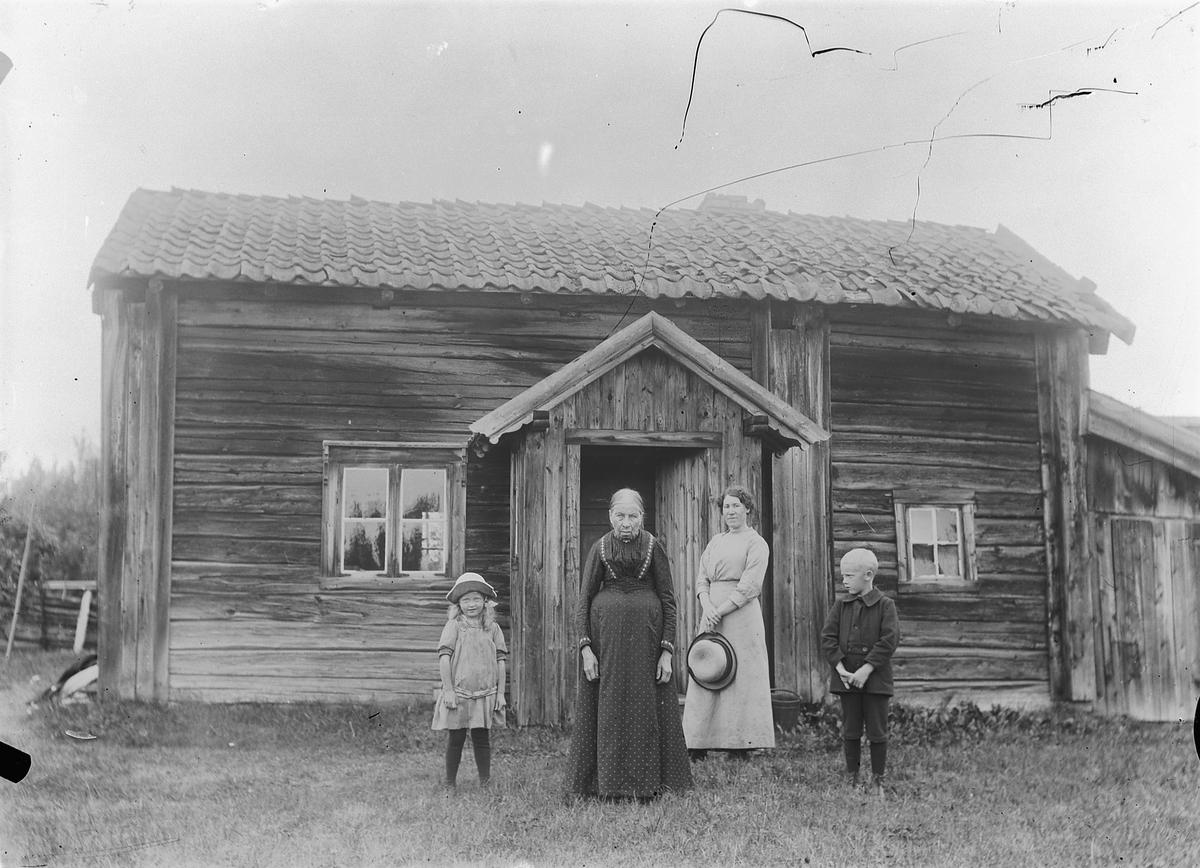Mina Skraastad, To kvinner og to barn foran et hus.