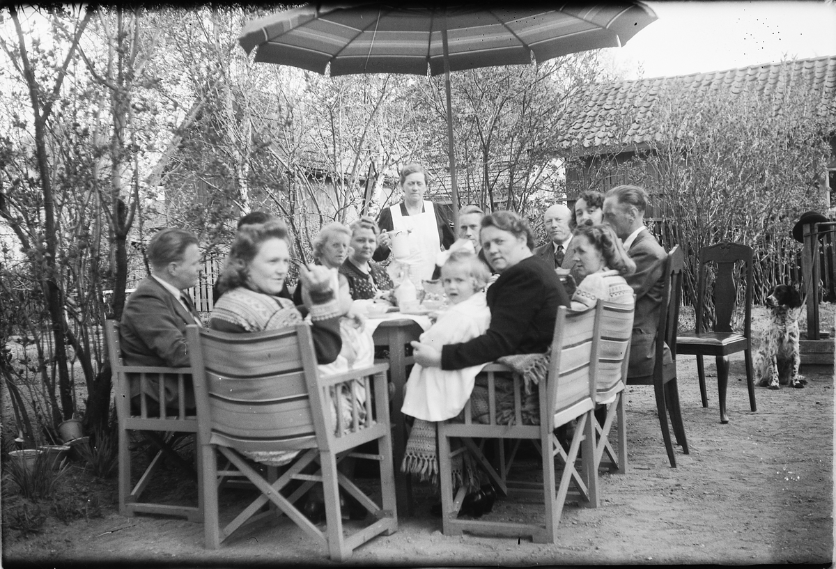 Håkon Prestkværn, Ukjent familiegruppe sitter rundt hagebord. Hageselskap. Kaffeselskap. Mannen helt til høyre i bildet (med siden til fotografen) er Paul Pettersen. Kvinnen ved hans venstre side (m. kaffekopp) er Martha Pettersen (f. Prestkværn), hans hustru.