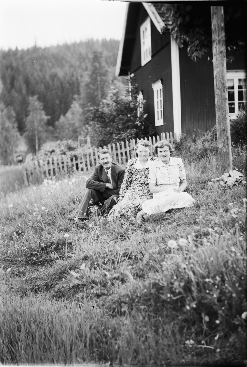 Håkon Prestkværn, Ukjent mann og to kvinner i gresset foran et hus.