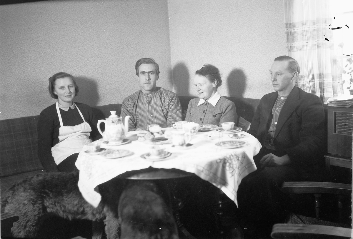 Håkon Prestkværn, Interiør, stue med radio. Ukjente personer rundt kaffebordet.
