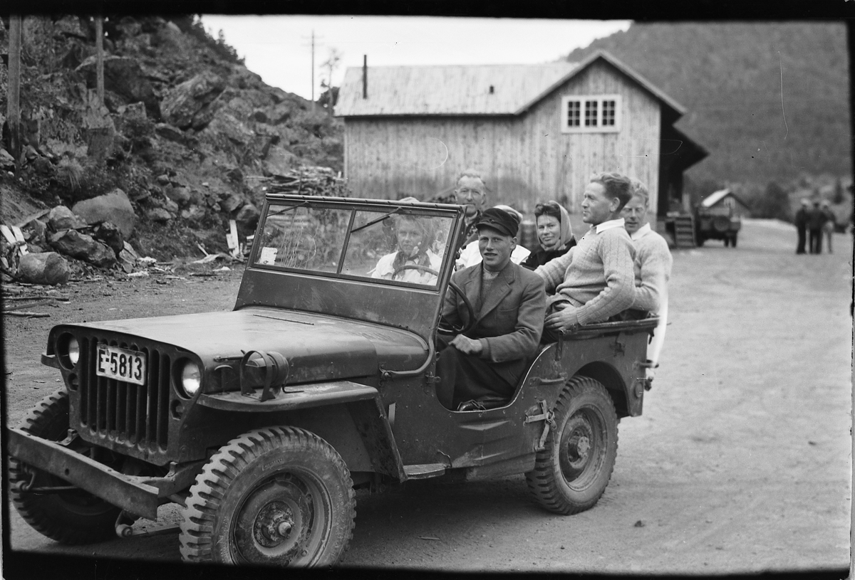 Håkon Prestkværn, Jeep, E-5813. Bil med mange ukjente personer, bygning i bakgrunnen.