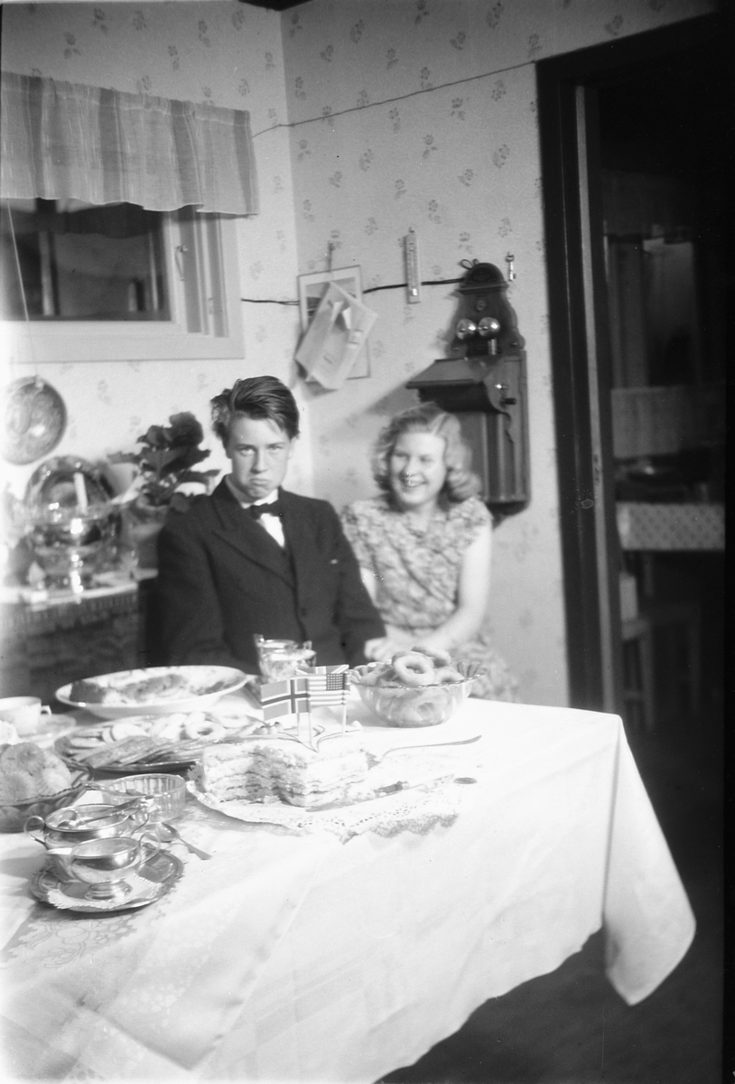 Håkon Prestkværn, Ukjent gutt og jente sitter ved et bord med kaker og smultringer.