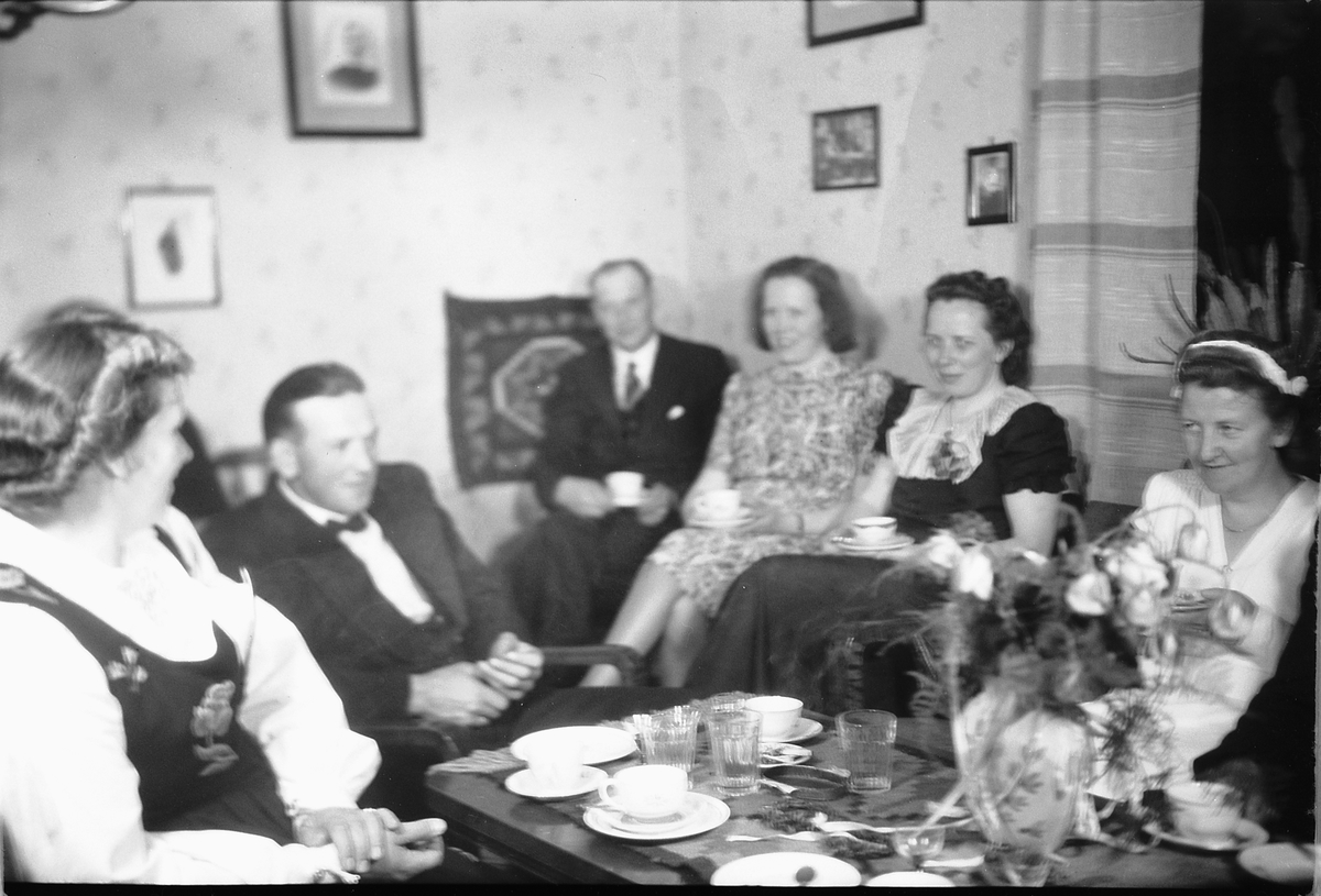 Håkon Prestkværn, Interiør, stue. Ukjente personer sitter rundt et bord og drikker kaffe.
