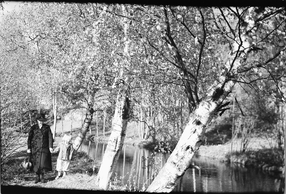 Håkon Prestkværn, En eldre kvinne og ei jente langs en elv i skogen.