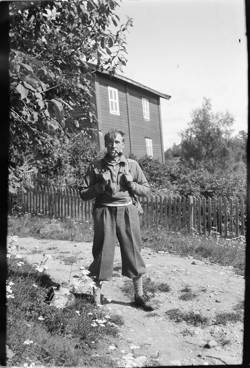 Håkon Prestkværn, Ukjent mann med nikkers, sekk og pipe på en vei ved et hus.