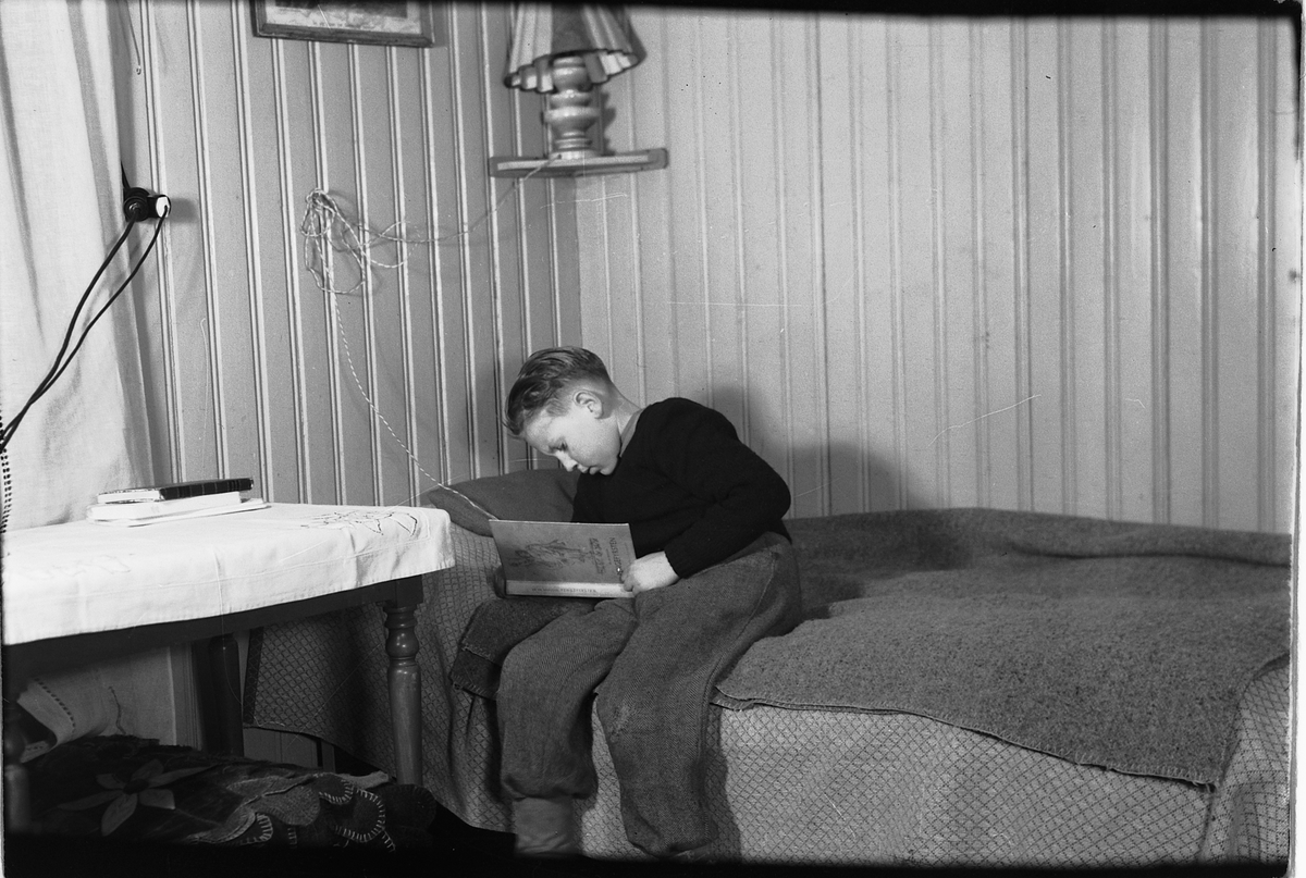 Håkon Prestkværn, Interiør, stue. Gutt sitter på soafen og leser ei bok.