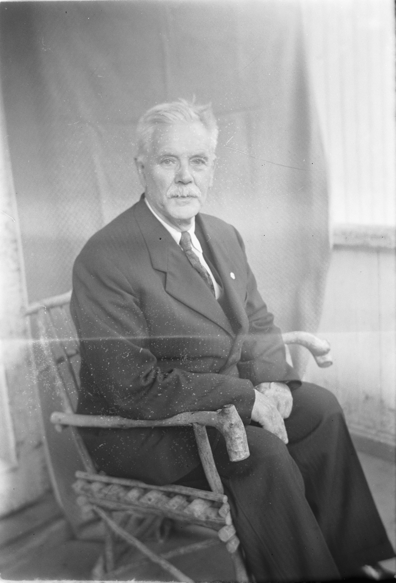 Håkon Prestkværn, Eldre mann i dress sitter på en stol.