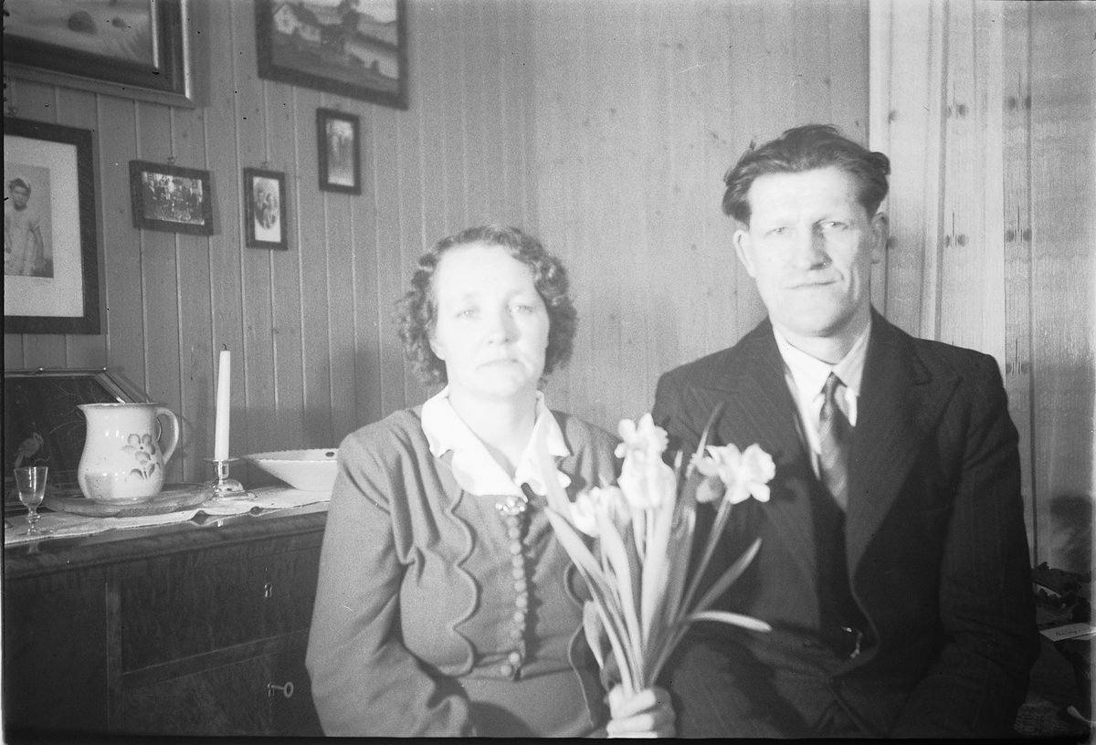 Håkon Prestkværn, Interiør, stue. Ukjent kvinne med blomster og ukjent mann.