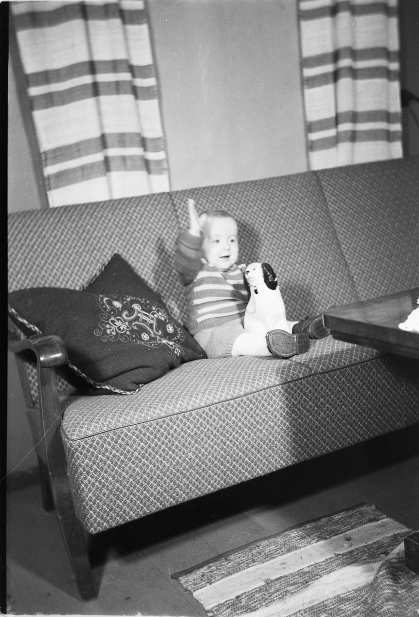 Håkon Prestkværn, Interiør, stue. Baby i en sofa med en leke.