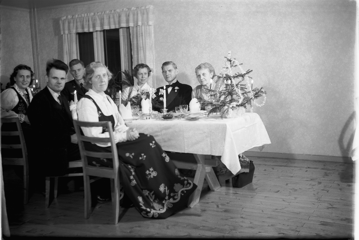 Håkon Prestkværn, Interiør, stue. Ukjent gruppe mennesker rundt et bord med kvinner i bunad.