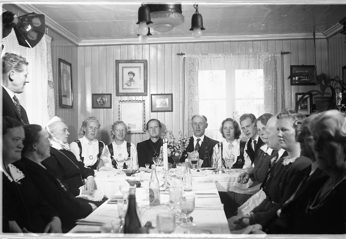 Håkon Prestkværn, Interiør, stue. Stor gruppe menn og kvinner samlet rundt dekket bord.