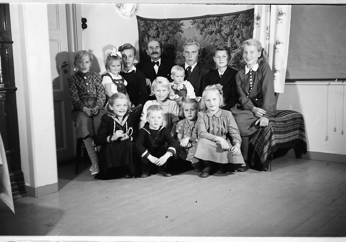 Håkon Prestkværn, Interiør, stue. Gruppe barn samlet rundt en eldre mann.
