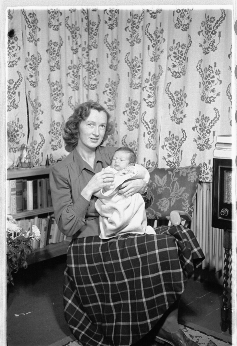 Håkon Prestkværn, Interiør, stue. Kvinne med en baby på fanget.