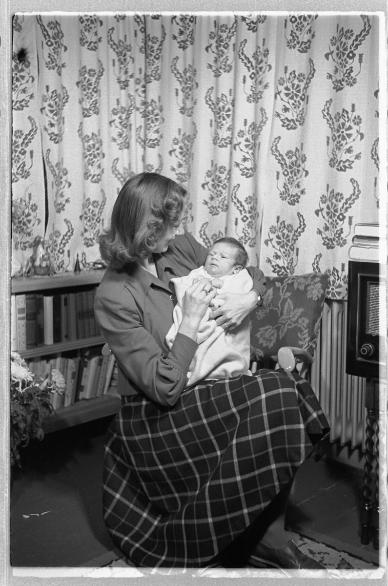 Håkon Prestkværn, Interiør, stue. Kvinne med en baby på fanget.