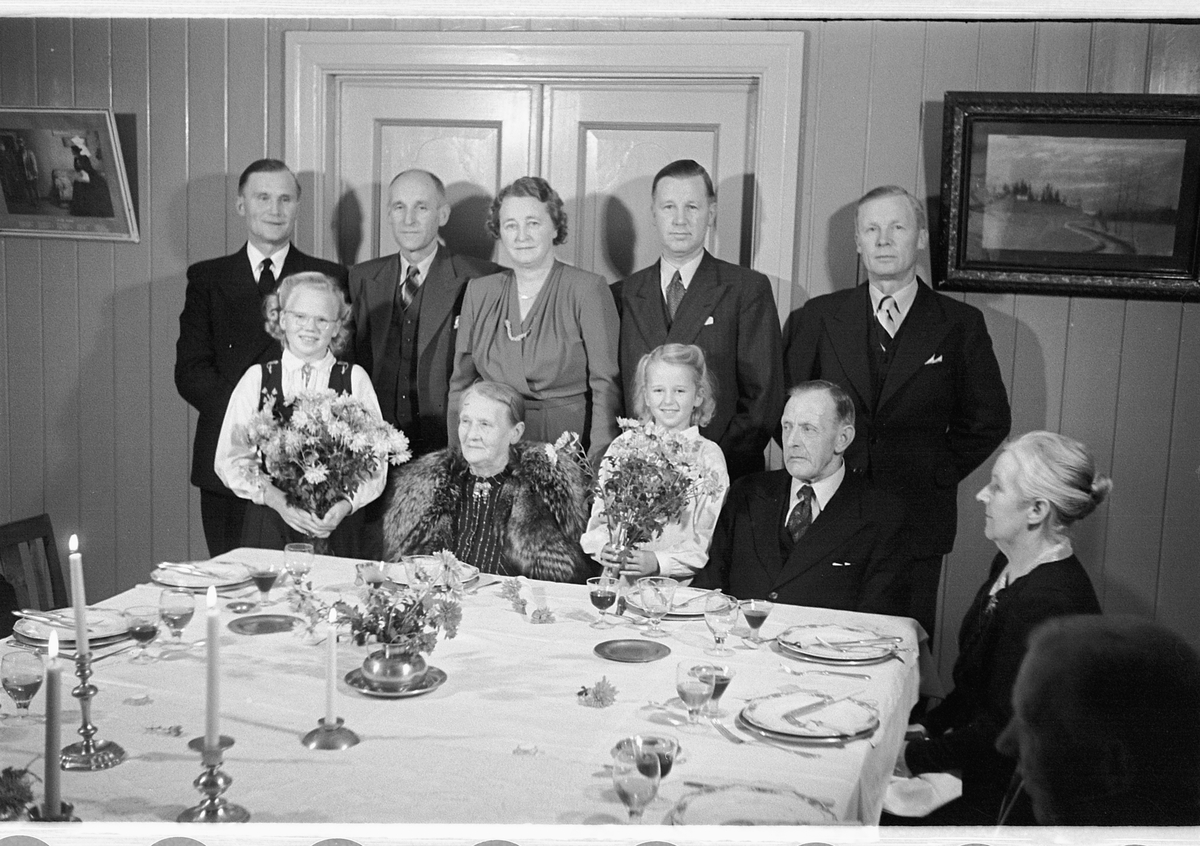 Håkon Prestkværn, Interiør, stue. Familiegruppe samlet ved et dekket bord.