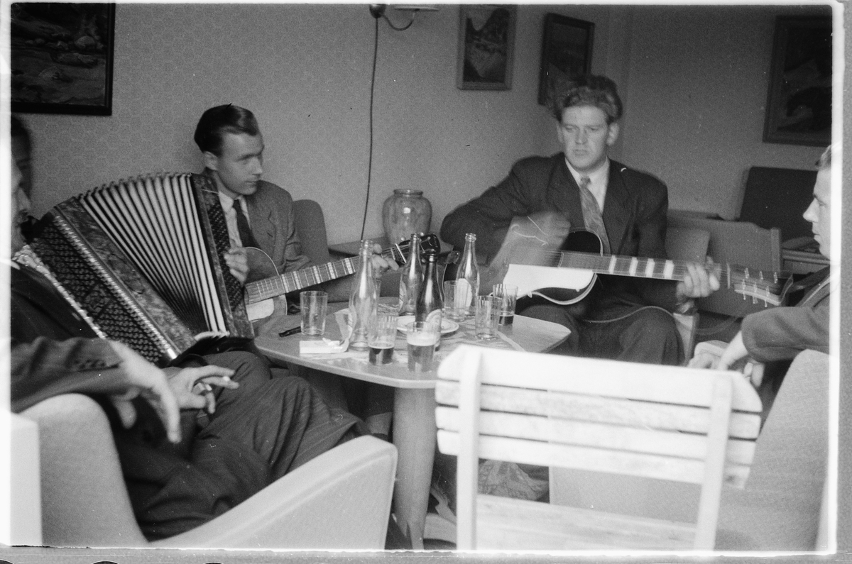 Håkon Prestkværn, Interiør, stue. Tre menn samlet rundt et bord spiller gitar og trekkspill. T. h. Ulf Eller Leif??)Sæhli på gitar. Mener å gjenkjenne Ulf Sæhli ved et annet fornavn. Leif. Kan jo være noen som er veldig lik ham, men han her likner veldig på Leif.