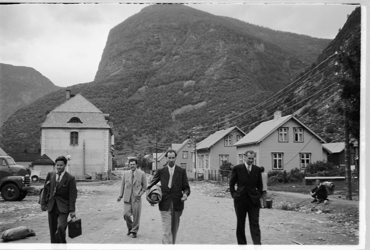 Håkon Prestkværn, Fire menn med hus i bakgrunnen. Storevegen, Øvre Årdal, Sogn og Fjordane.