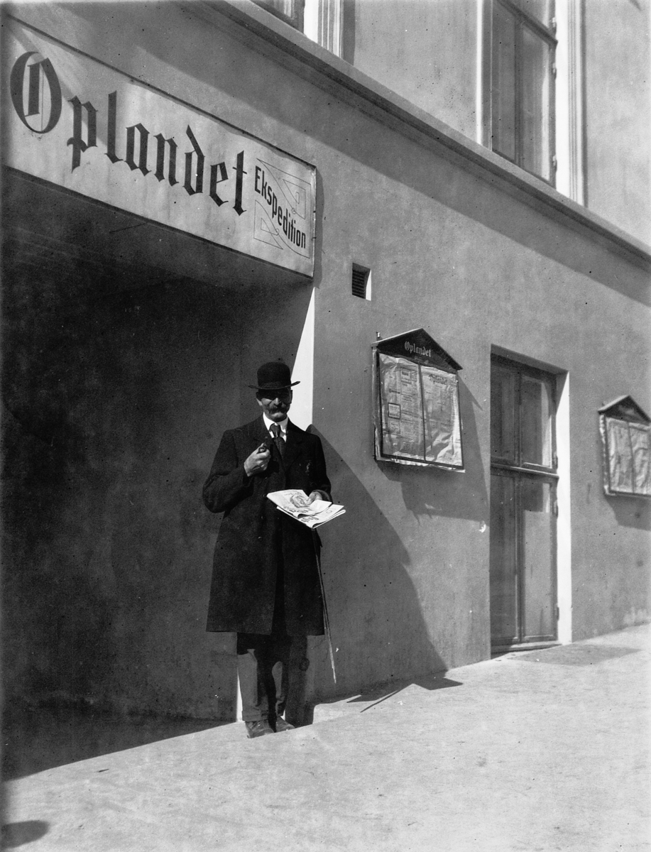 Ragnvald Andersen, Mann i dress leser avis utenfor bygget til Oplandet Ekspedition.