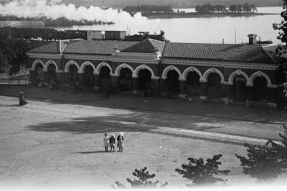 Hans Emil Erichsen, Stortorget, Hamar. Basarbygningen med et damptog i bakgrunnen. Basarbygningen sto ferdig i 1896.