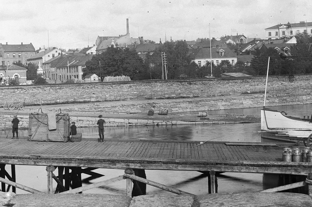 Hans Emil Erichsen, Hamar brygge med dyrekasser, sprittønner og melkespann. Basarbygningen i bakgrunn. Bebyggelsen rundt Stortorget.