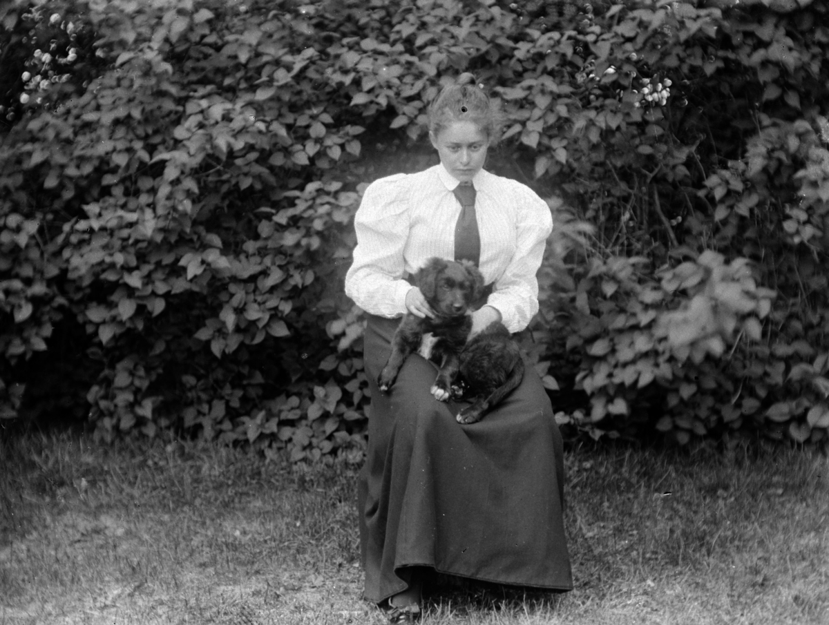 Martin Finborud, En kvinne, med en hund på fanget, sitter i en hage. Sofie Pihl (f Mellbye)?