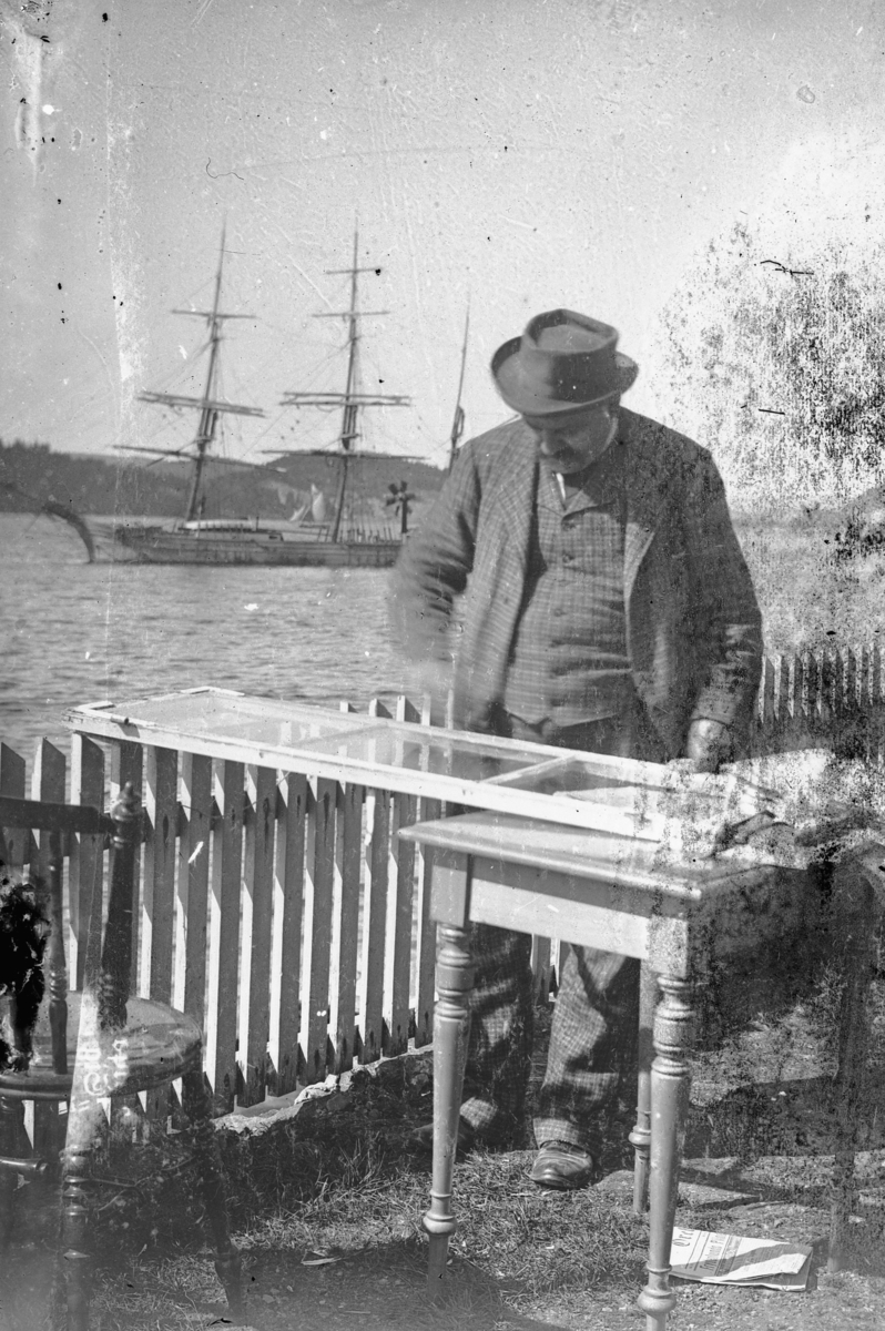 Hans Emil Erichsen, Ukjent mann reparerer vindu. Seilskute på sjøen i bakgrunn.