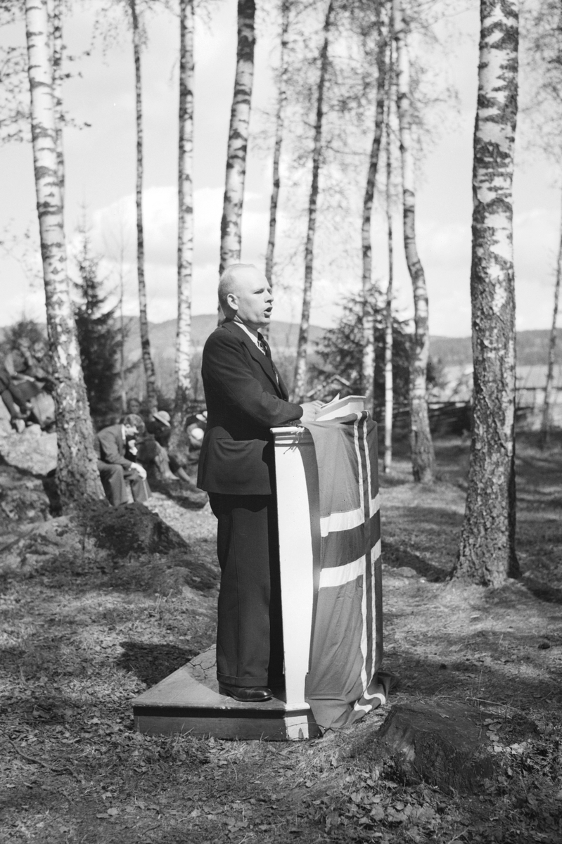 Håkon Prestkværn, Molunden i Moelv, ukjent mann holder 17. mai tale. Talerstol pyntet med norsk flagg.