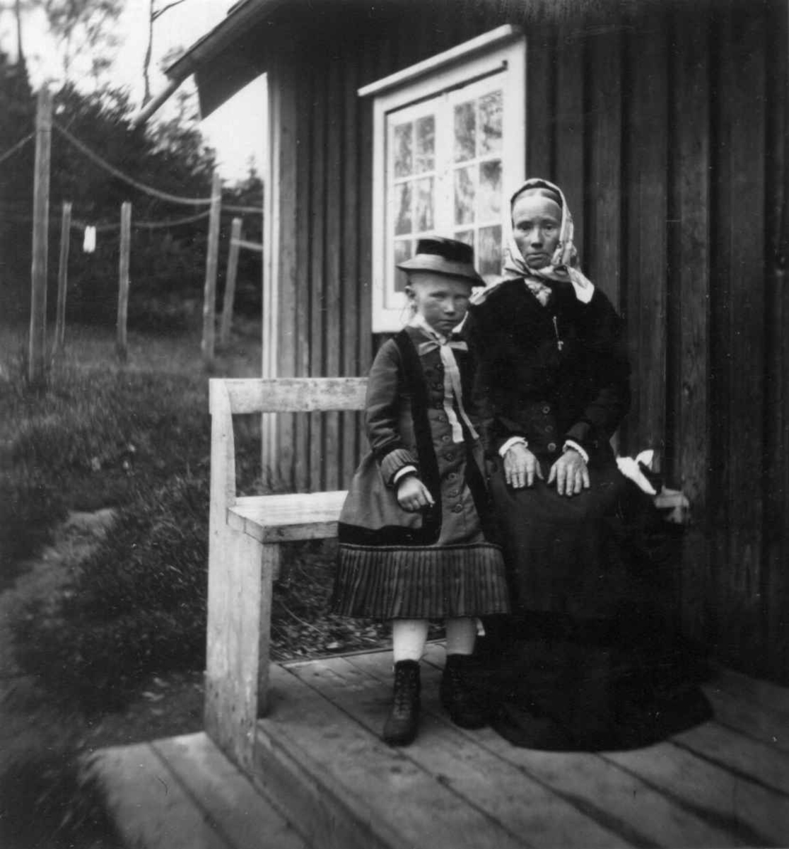 Fredrik Emil Faye, Husmannsfolk, kvinne og pike på benk foran hus. Fra portrettserie av personer som bodde på eller besøkte Dal gård, Ullensaker, fotografert av gårdens eier, kammerherre Fredrik Emil Faye (1844-1903) i årene 1875-1900.